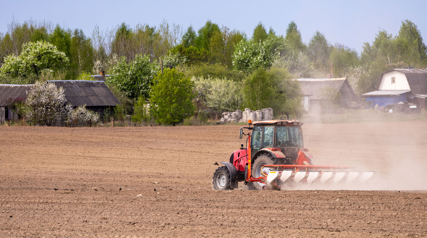 Semoir de semis direct moderne en action sur parcelle couverte de résidus, sillons visibles au premier plan, tracteur en arrière-plan, lumière contrastée et dynamique
